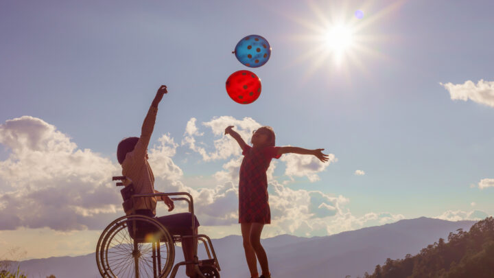child in wheelchair with balloons and other child standing