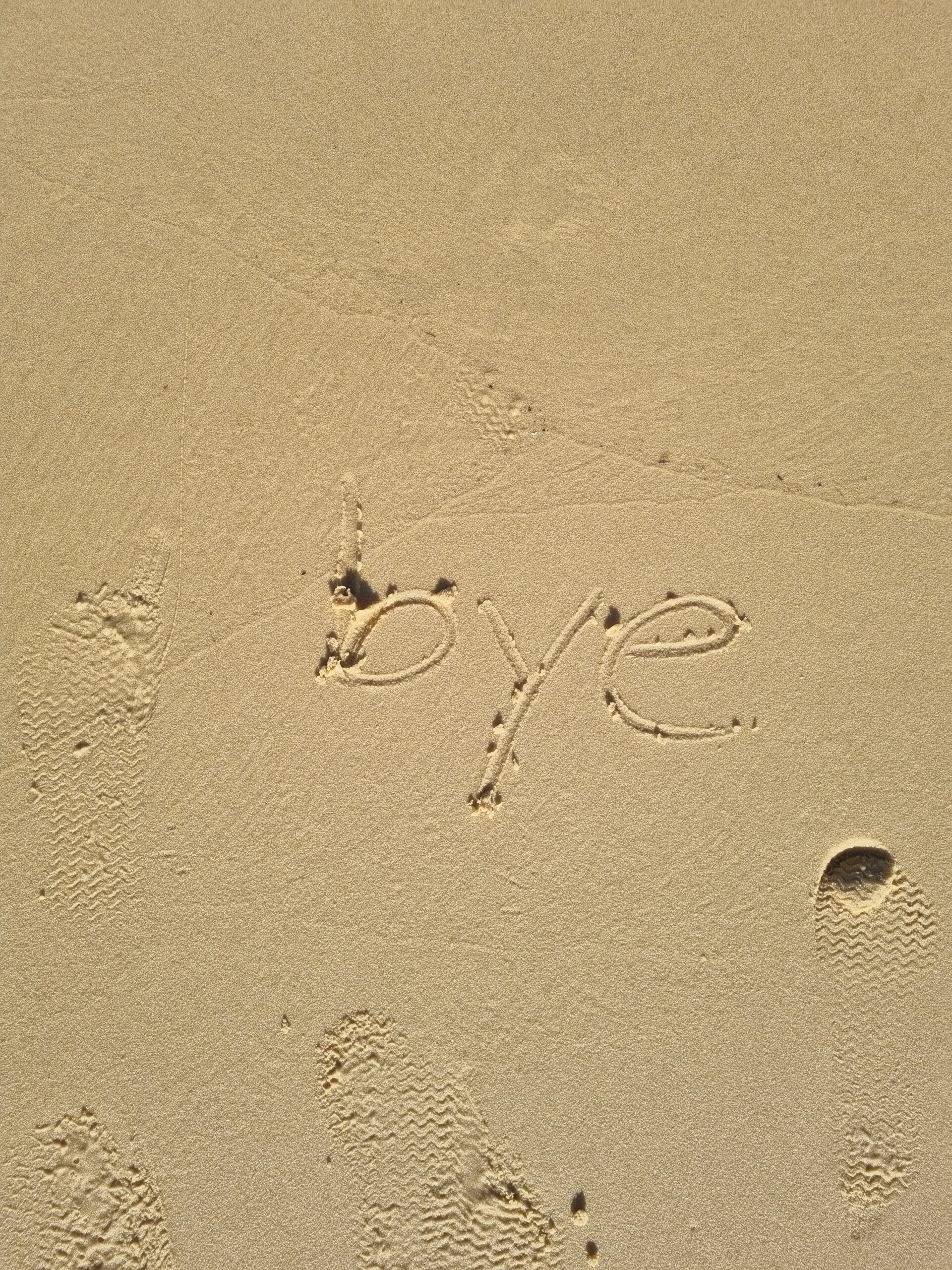 word 'bye' written in sand on beach